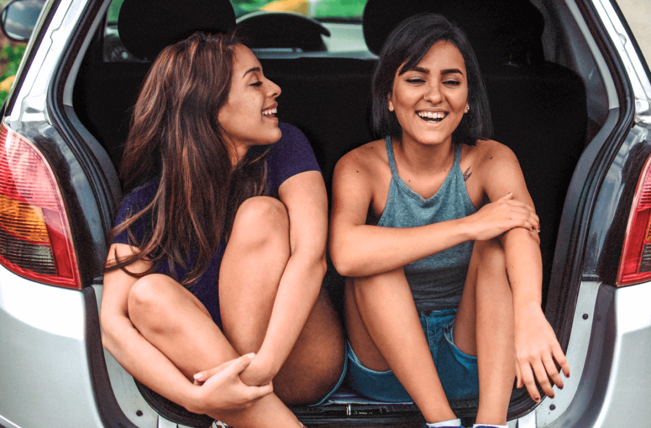 Two young woman smiling and sitting in the trunk of a SUV